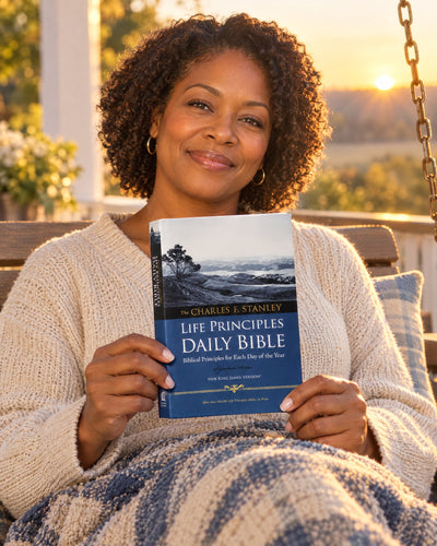 Woman holding the Life Principles Daily Bible NKJV on a porch at sunrise